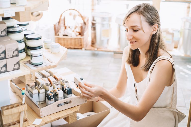 Empreendedora organizando sabonetes artesanais em loja de cosméticos, representando boas práticas de cadastro de produtos e controle de estoque.
