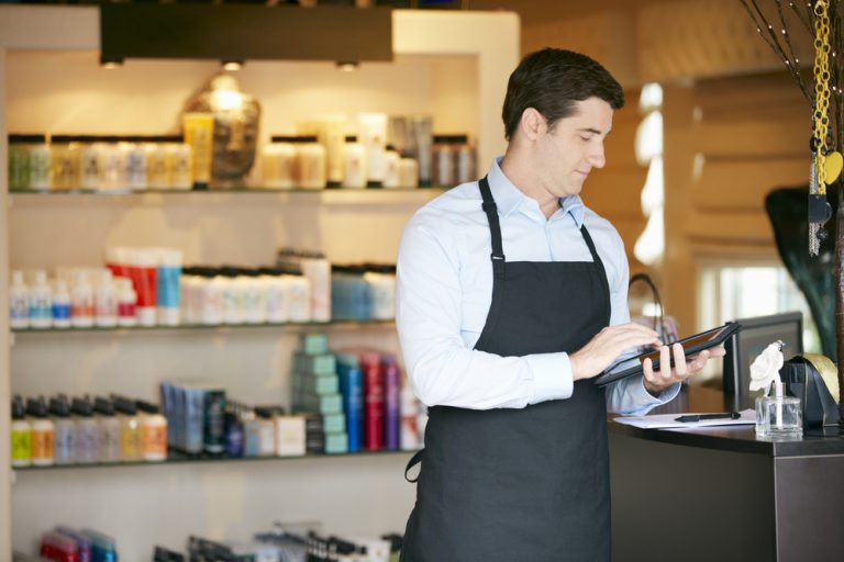 Homem usando tablet para gerenciar estoque e vendas em loja de cosméticos, representando o uso de ferramentas de gestão.