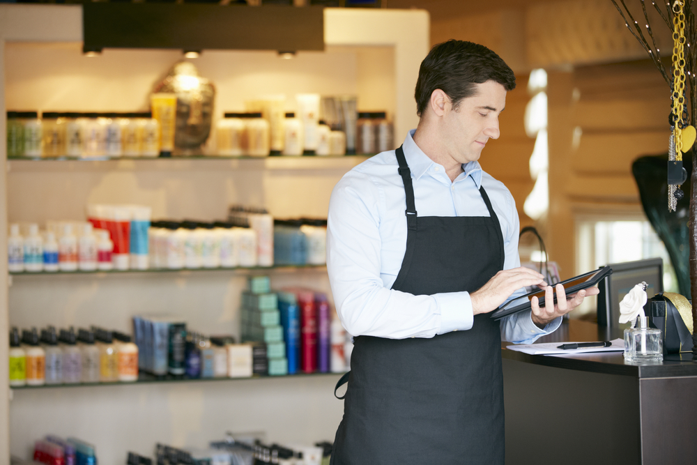 Homem usando tablet para gerenciar estoque e vendas em loja de cosméticos, representando o uso de ferramentas de gestão.