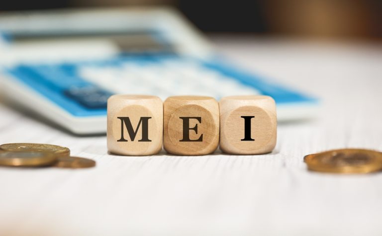Blocos de madeira com as letras MEI e moedas ao lado de calculadora, representando microempreendedor individual