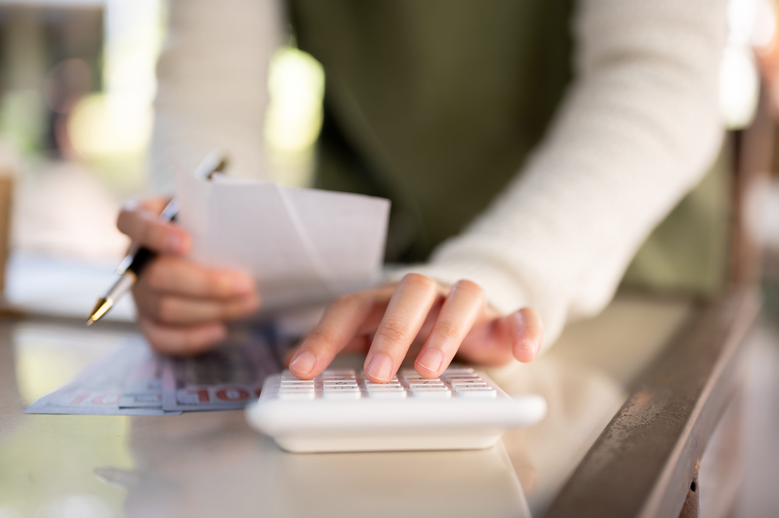 Pessoa calculando despesas com calculadora e anotando valores, representando organização financeira para pequenos negócios.