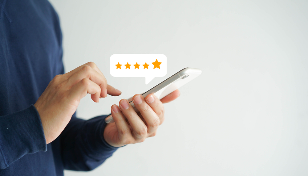 Pessoa avaliando um serviço com cinco estrelas no celular, representando um bom atendimento ao cliente.