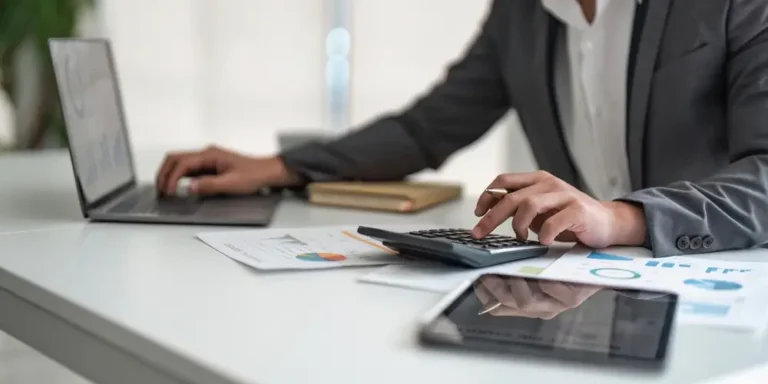 Pessoa utilizando calculadora e computador para analisar gráficos financeiros, representando o processo de como calcular preço de venda de produtos e serviços.