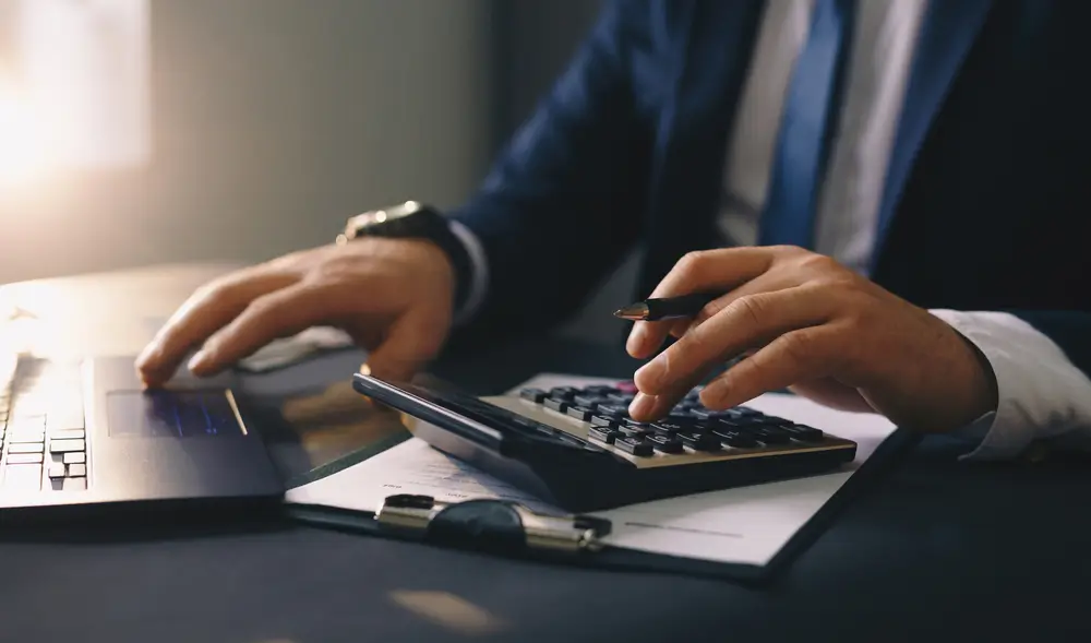 Empresário usando calculadora e notebook para calcular capital de giro e organizar finanças da empresa.