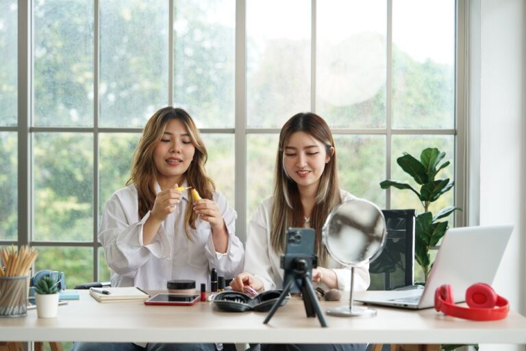 Duas mulheres gravando conteúdo para vender maquiagem online com produtos dispostos na mesa